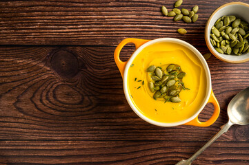Pumpkin soup in orange ceramic bowl, wooden background. Autumn food