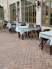 Rustic outdoor cafe terrace with wooden tables and checkered cloths by a stone building. Social gatherings, hospitality, and cultural atmosphere in Drvengrad.
