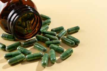 Spirulina capsules spilled in amber bottle on beige background. Dietary supplement, immunity boost. Selective focus