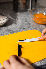 Chef's hands scraping vanilla beans for baking. Close-up on orange cut board.