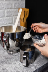 Closeup of woman pour wheat flour powder into mixing bowl with baking ingredients.
