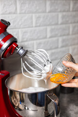 Pastry chef adding egg yolk in the red mixer bowl. Preparing cooking for dinner guests