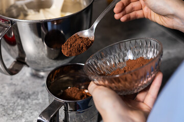 Closeup of woman  pour cocoa powder into mixing bowl with baking ingredients.