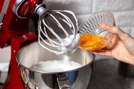 Pastry chef adding agg yolk in the red mixer bowl. Preparing cooking for dinner guests