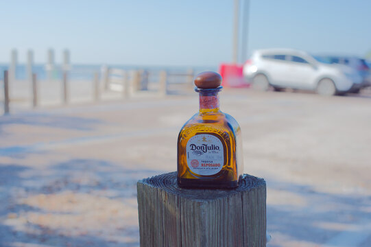 Small bottle of Tequila Don Julio Bottle Resting on Weathered Post at the Beach With Seascape Background. Editorial Use Only September 20, 2025 St. Petersburg, FL USA. Blurred beach and parked cars in