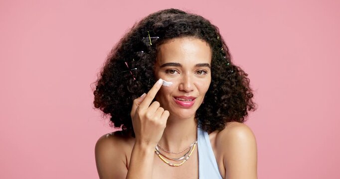 Face, cosmetology and woman in studio with cream, hydrate and spf lotion in skincare. Beauty, smile and female person with moisturizer, sunscreen protection and facial care on pink background.