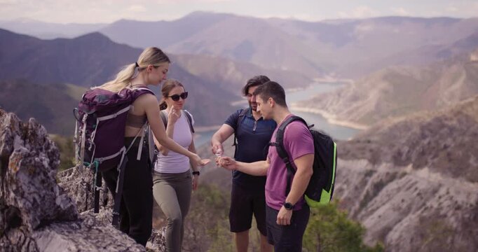 Group of four friends sharing a fun moment while hiking in the mountains. They are exchanging high fives with a beautiful lake and mountains in the background.