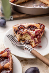 Homemade The New York Times plum cake. Slice of autumn fruit pie in a plate with fork on beige textured background. Home cooking, recipe