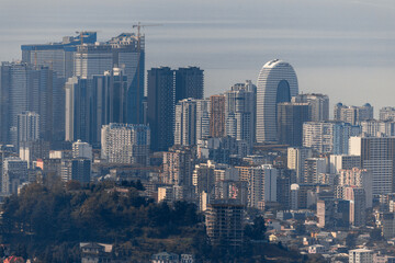 Fototapeta premium A cityscape with tall buildings and a blue sky. Panorama of Batumi from the mountains. Skyscrapers and buildings.