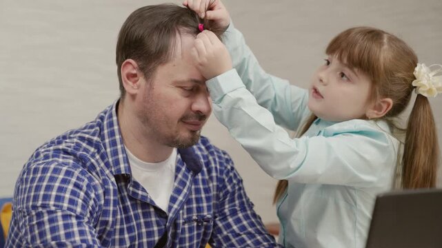 Dad is a freelancer who works remotely from home, a little daughter always gets in the way, plays. The child combs his father's hair and does his hair. Raising children at home with parents