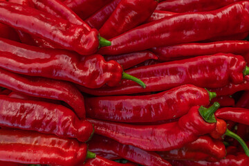 Close-up macro of stacked red long peppers (Capsicum annuum) at a produce market display, ripe glossy skin and green stems, harvested pile of fresh peppers, natural outdoor light, shallow depth of fie