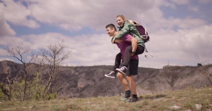 Two friends having fun outdoors with a joyful piggyback ride against a scenic mountain backdrop, embodying adventure and camaraderie. - Powered by Adobe
