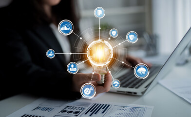 A business professional engages with a laptop while holding a light bulb, surrounded by digital icons symbolizing technology, finance, and innovation in a modern office. Crux