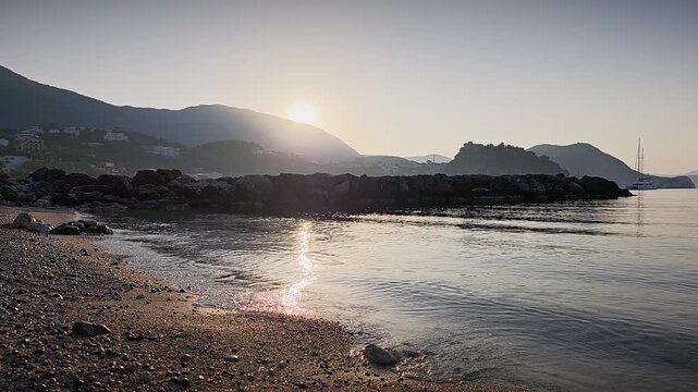 Sunrise over Parga Greece captured from tripod. Golden light reflecting on Ionian Sea, silhouettes of mountains and boats create cinematic Mediterranean morning atmosphere.