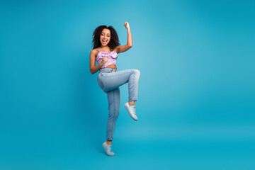 Young woman jumping with joy in casual stylish outfit against a bright blue background showcasing happiness energy fashion and lifestyle