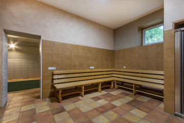 A spacious spa room decorated with brown tiles. A long wooden bench and the entrance to the sauna.