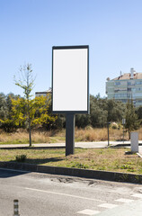 Vertical blank billboard mockup on a roadside in Lisbon, Portugal. Outdoor advertising display with empty white space for design or promotional content, set against a clear blue sky, trees