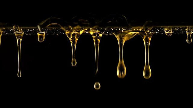 Flowing viscous golden liquid drips downwards against a stark black backdrop, showcasing detailed macro droplets and reflecting light, creating a visually appealing abstract arrangement.