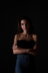 Naklejka premium Portrait of a woman with arms crossed in a dark setting showcasing confidence and poise