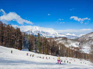 A wide slope with large group of middle school students learning to ski on a Mount Myoko in the background (Madarao, Nagano, Japan)