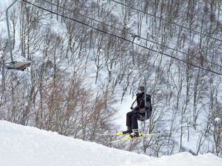 Winter scene with a skier on a single ski lift surrounded by trees (Madarao, Niigata, Japan)