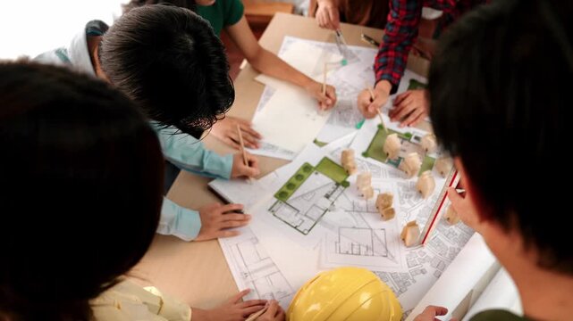 Architect and safety engineer discussion about building construction use blueprint on table with architectural document, measurement tool and wooden block scatter around at modern office. Delineation.