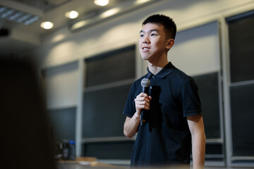 Young man speaking confidently with a microphone in a university lecture hall. Represents public...
