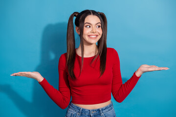 Young woman in casual red outfit with ponytails gesturing on blue background, expressing lively...