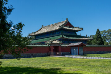 Obraz premium A majestic traditional Chinese temple or hall with an intricate green tiled roof and a perimeter red wall. The historic structure is set against a blue sky and green lawn, conveying culture 