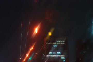 A blurry view of night traffic and streetlights seen through a rainy car windshield.
