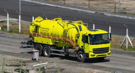 Bright yellow vacuum truck parked on a road near construction. Industrial vehicle used for liquid waste removal, maintenance or cleaning services