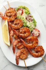 Skewers with tasty grilled shrimps, salad and lemon slice on white marble table, top view. Delicious seafood dish