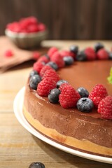 Delicious chocolate cheesecake with berries on wooden table, closeup