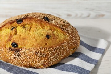 Loaf of fresh bread with sesame seeds and raisins on white wooden table, closeup