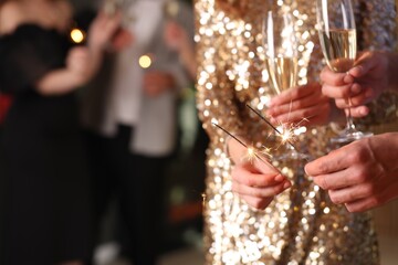 Friends celebrating New Year with sparklers and wine glasses indoors, closeup