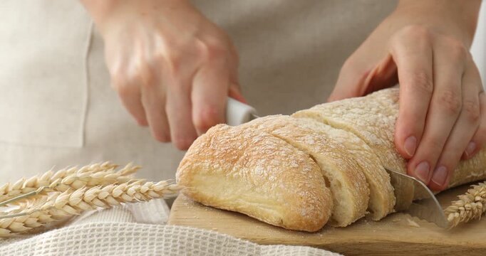 Woman cutting fresh crispy ciabatta at table, closeup