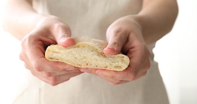 Woman squishing piece of fresh ciabatta on light background, closeup