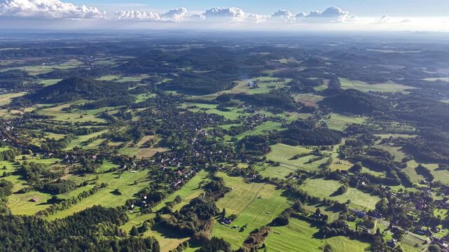 An aerial shot beautifully captures vibrant green fields and quaint little villages beneath a bright, cloudless sky