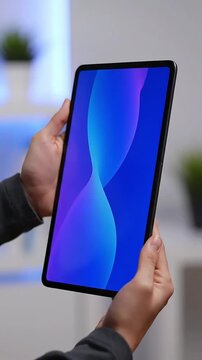 Close up of hands holding a modern digital tablet device with a vibrant blue gradient screen showcasing technology and digital interface in a sleek vertical ori