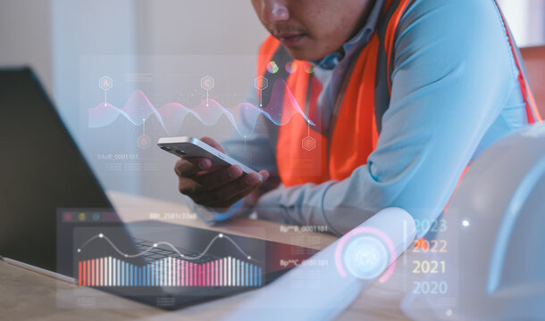 Engineer using smartphone and computer with futuristic charts interface for automation and monitoring Futuristic industrial automation, smart factory technology, monitoring innovation concept