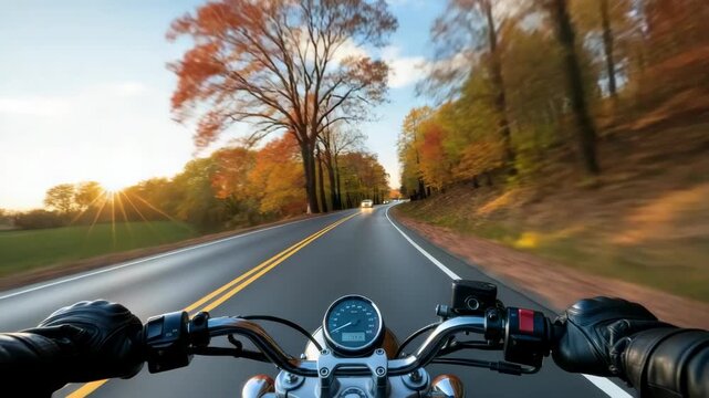 POV shot from motorcycle on scenic autumn road Riders gloved hands are on handlebars speedometer visible Golden sun rays illuminate fields while vibrant trees line the winding path