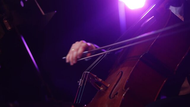 Harmony in Strings: A musician's hand gracefully draws a bow across the strings of a cello, producing a symphony of resonating sound under a spotlight.