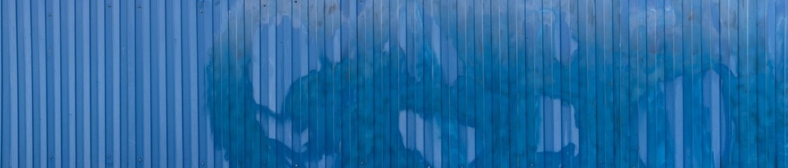 A textured blue metal corrugated fence wall background panorama with vertical lines and abstract...
