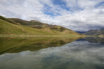Serene mountain landscape with calm water reflecting clouds and hills