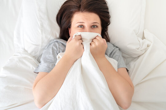 Portrait of scared young woman in bed hiding under blanet