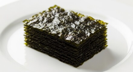 Stacked sheets of dark green, dried seaweed snacks on a white plate
