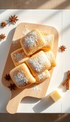 Stacked golden buns dusted with sweet confectioner's sugar presented on a light wooden board with spices under bright sunlight