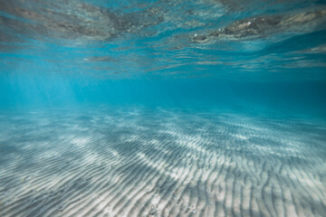 Scenic underwater view of sandy seabed with sun rays shining through clear blue water