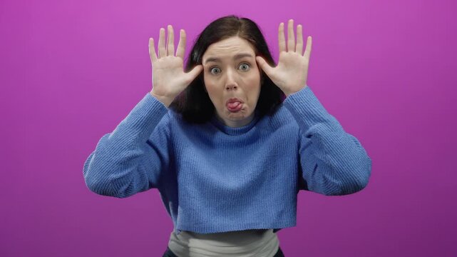 Woman expressing emotions against pink background with brunette hair and blue sweater, acting exaggerates sadness and playfully mocks in vibrant scene highlighting quirky mood.