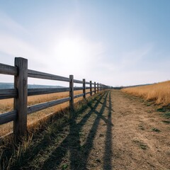 A tranquil pathway meanders through a golden meadow, bordered by a rustic wooden fence. The scene captures the beauty of nature under a clear sky, evoking feelings of peace and openness.